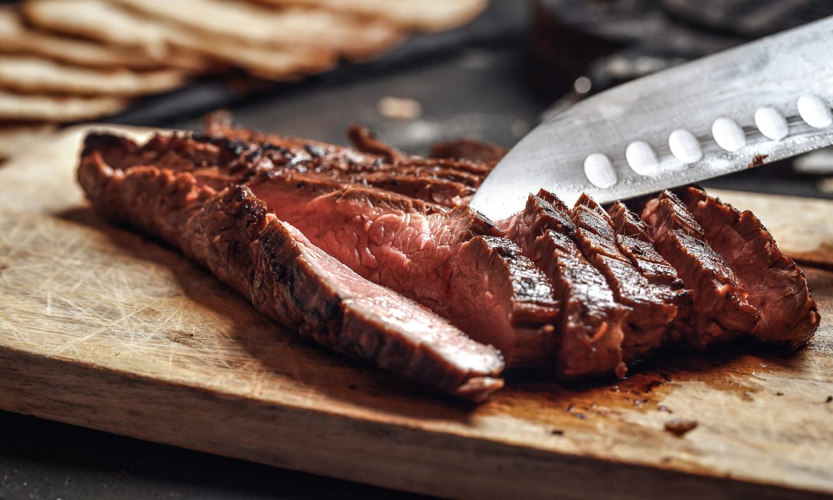 Cutting in slices flank steak on wooden cutting board