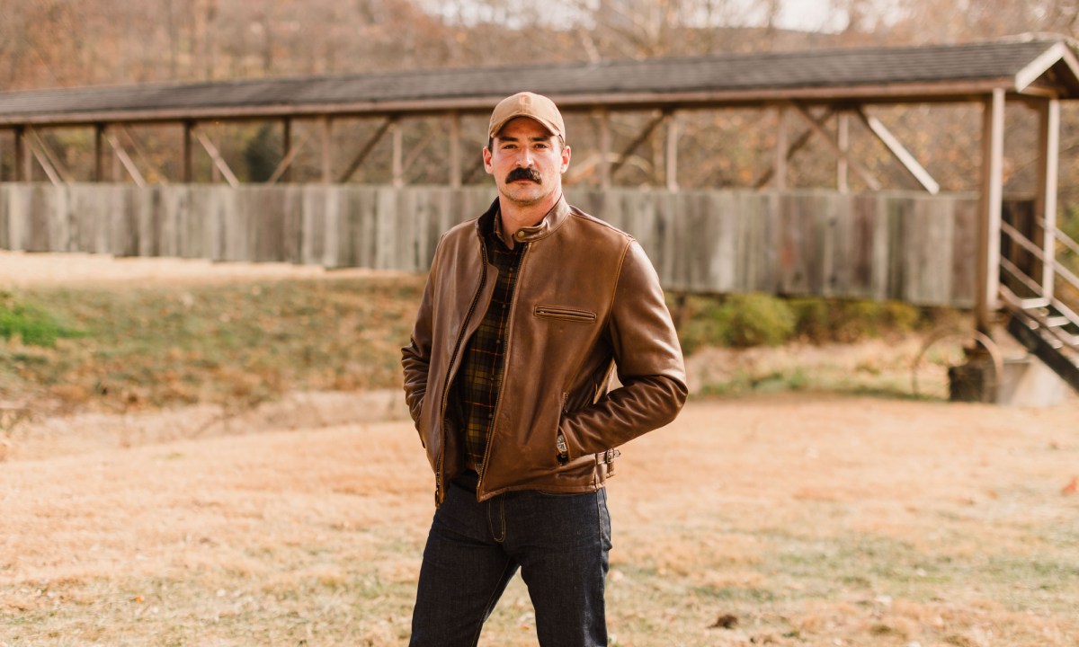 A man standing facing the camera with his hands in the pockets of a Ball and Buck x Schott NYC Leather Jacket.