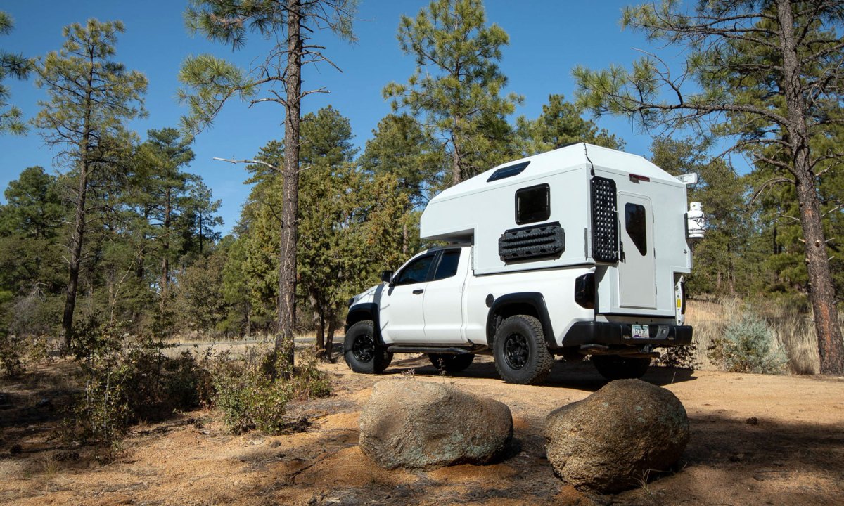An AT Overland Aterra Slide-In truck camper setup in a wooded campsite.