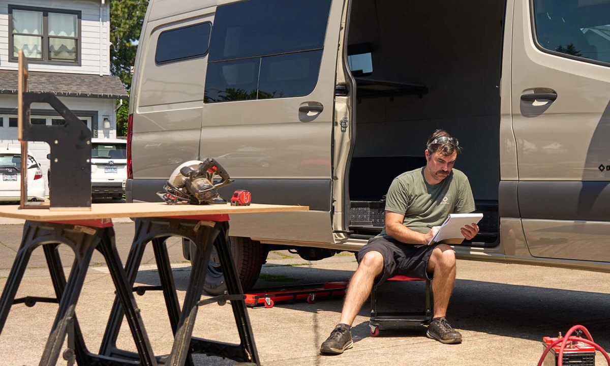 Young man planning out a campervan build while sitting inside an Outside Van Baseline adventure van.