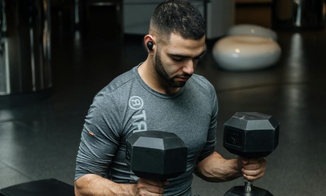 Man sitting on bench in gym holding weights dumbbells