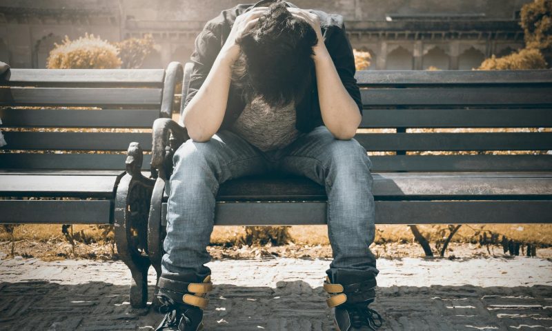 Man depressed stressed sitting on bench outside