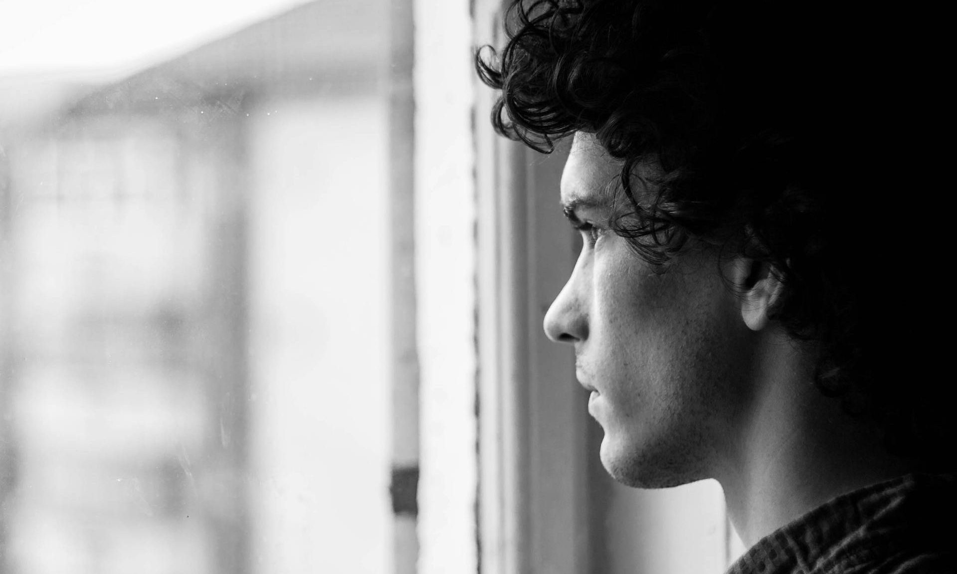 man reflective looking out the window thinking sad