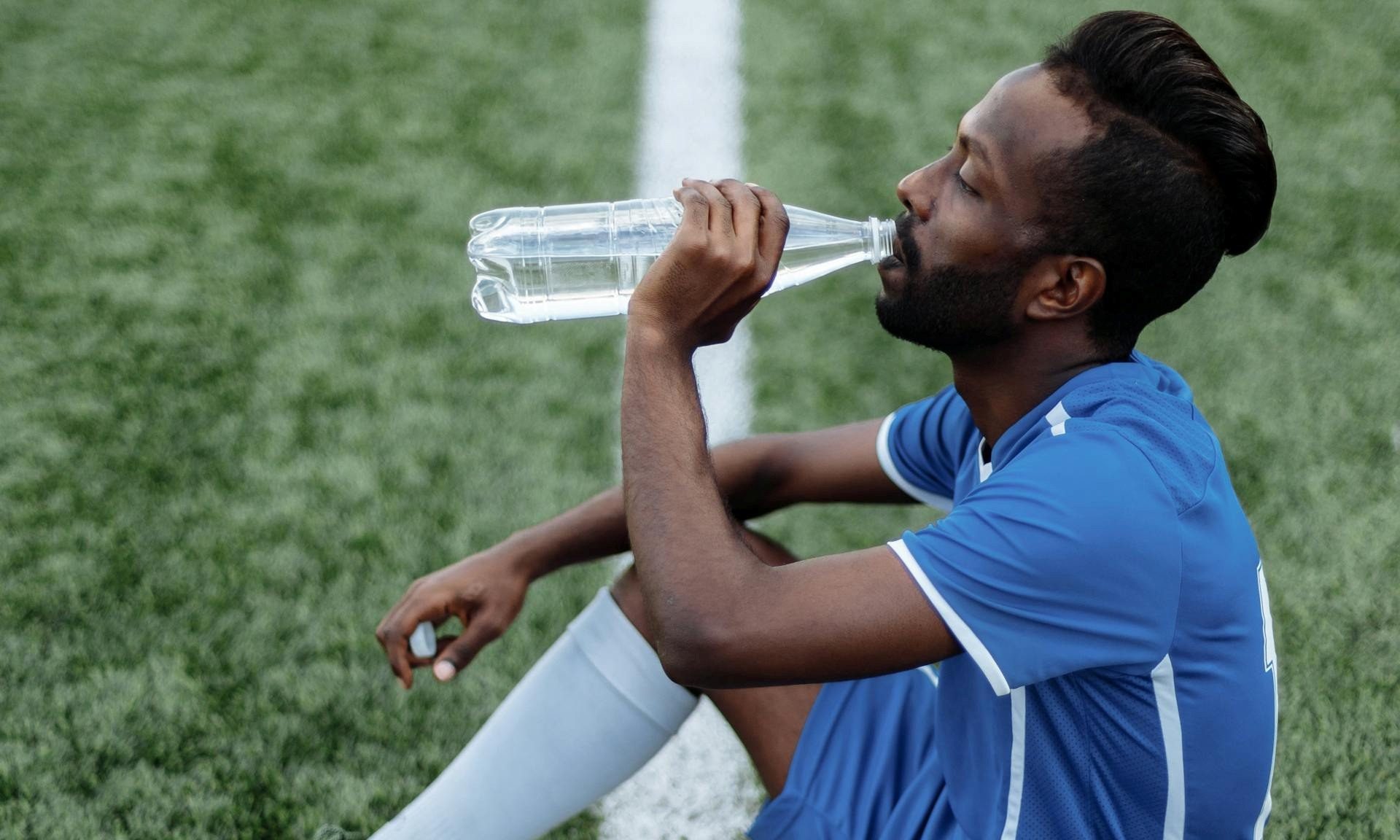 mansitting down on football field drinking water bottle