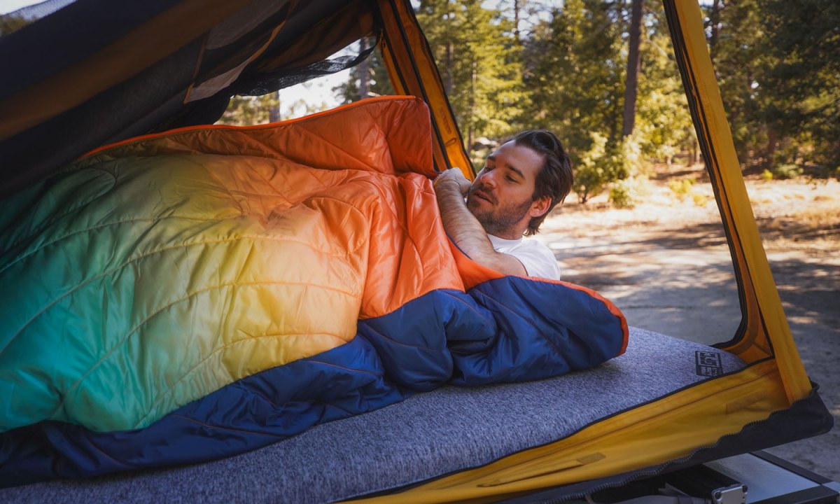 Young man camping inside a rooftop tent with Rumpl's Wrap Sack sleeping bag.