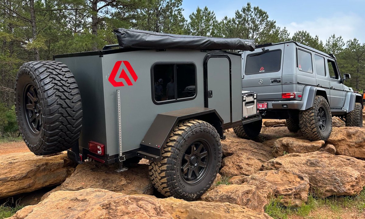 A gray SUV towing a Runaway Campers Venturist teardrop travel trailer down a rocky trail.