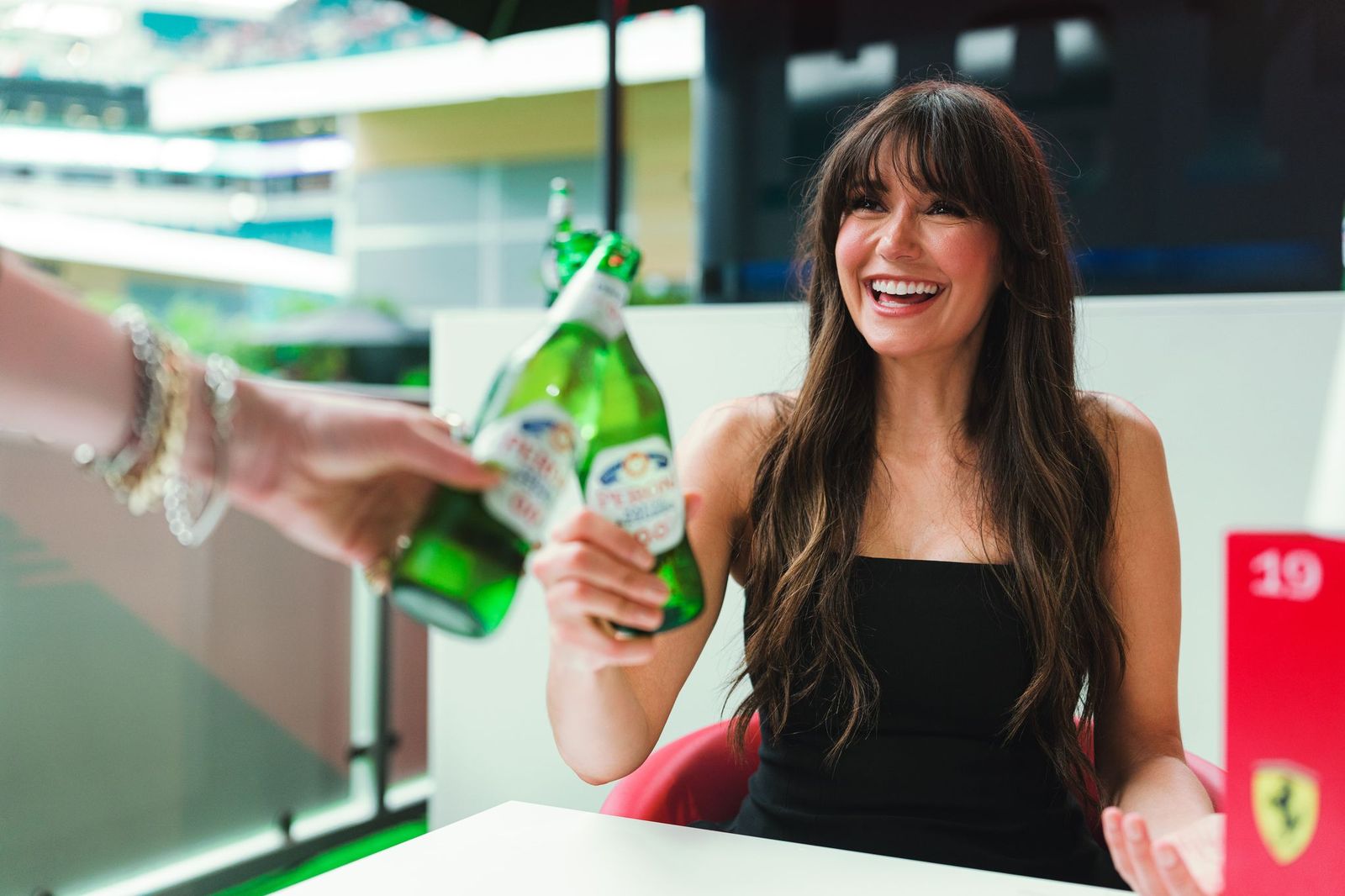 Nina Dobrev clinks bottles and smiles.
