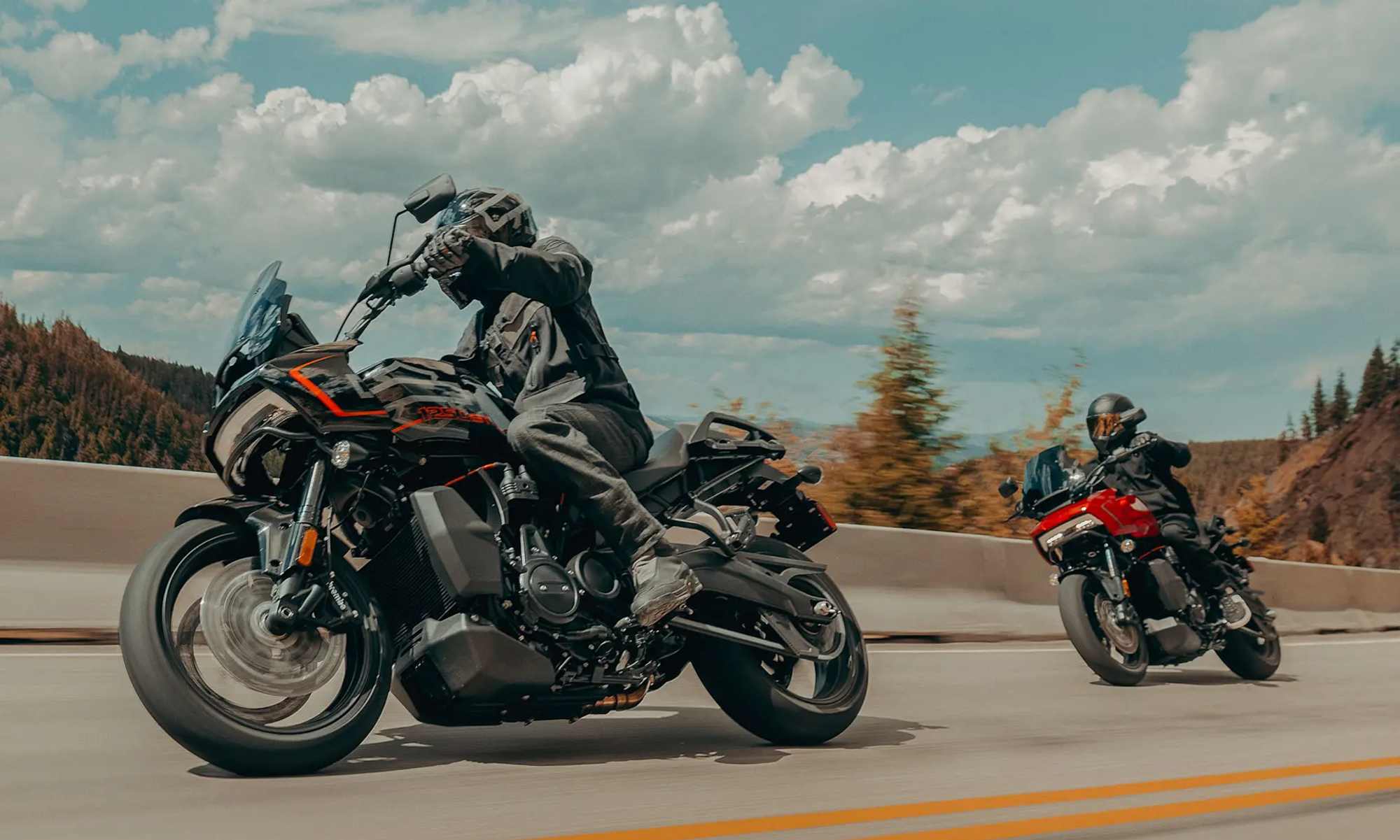 Two 2025 Harley Davidson Pan America 1250 STs on a curving road with mountains in the background.