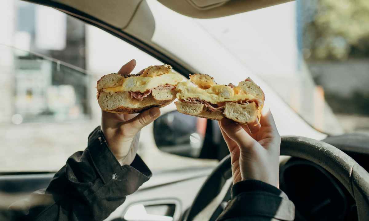 person holding a bagel sandwich in a car