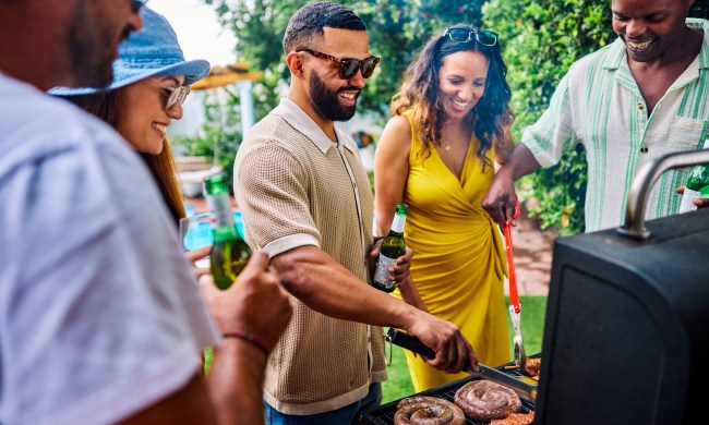 Diverse group of friends and family grilling sausages, corn, and chicken skewers at a barbecue party. Outdoor social gathering. Summer food and cooking concept.