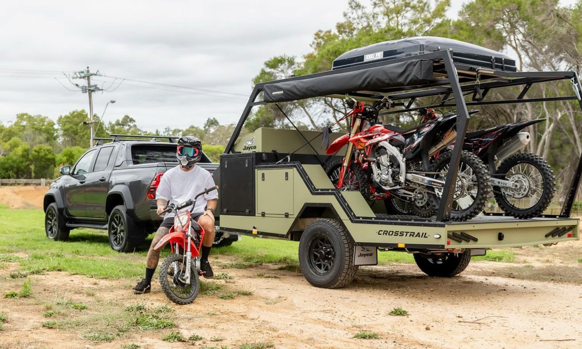 Dirt bike rider parked next to a Jayco Crosstrail off-road toy hauler RV.