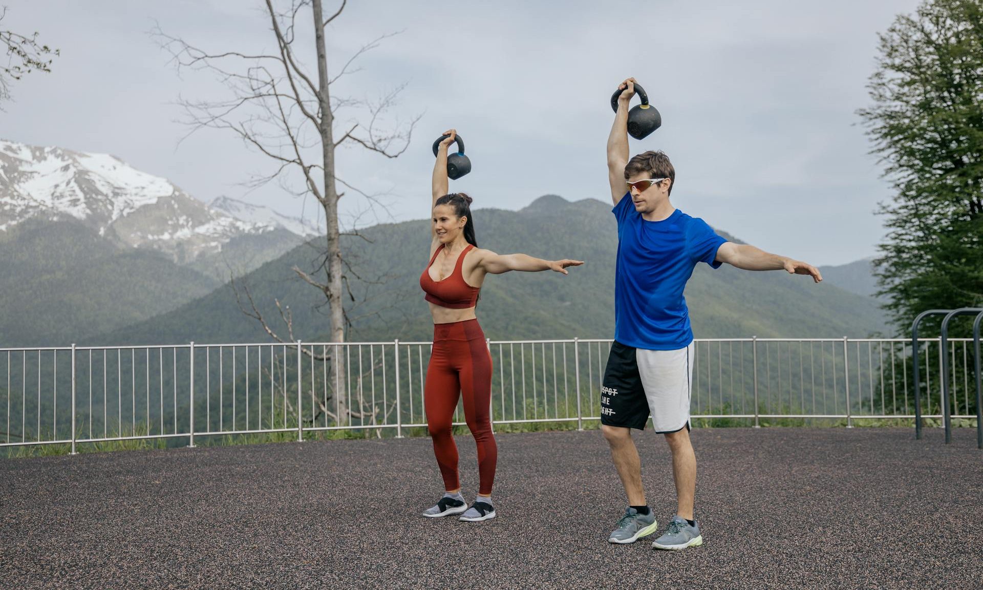 man and woman outside holding kettlebell overhead