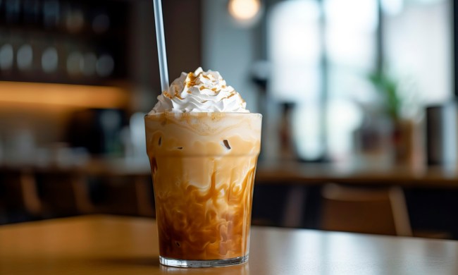Glass of iced coffee topped with a generous dollop of whipped cream, a caramel drizzle, and a straw for sipping.