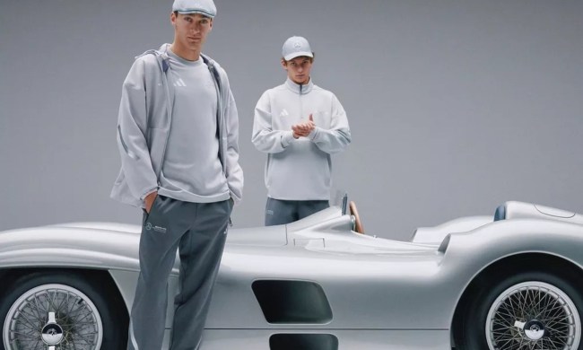 F1 drivers George Russell and Kimi Antonelli wearing Mercedes fan wear with a Mercedes-Benz W196 racecar.