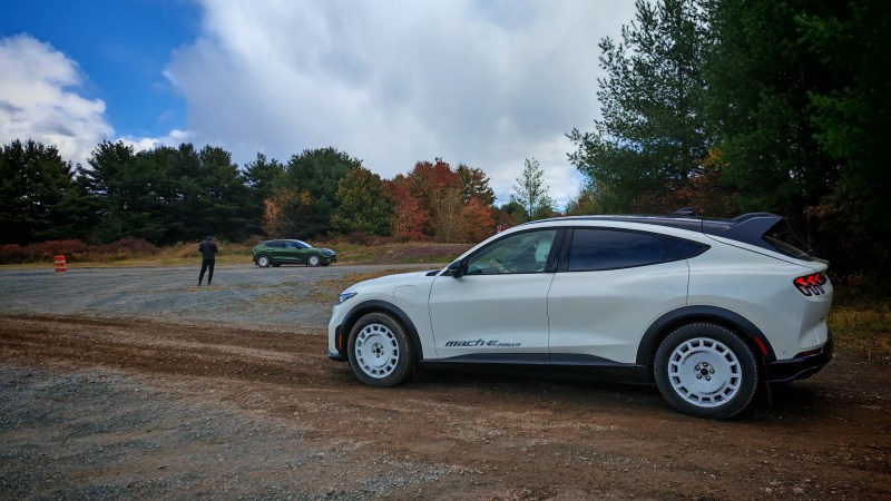 A Mustang Mach E rally on a dirt path near a gravel car park