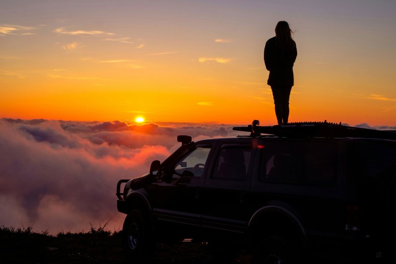 Girl standing on top of an overlanding SUV looking out over the clouds.