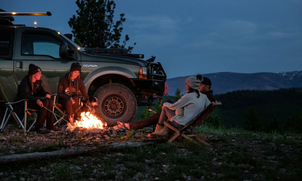 Four young campers sitting around a campfire next to an overlanding pickup truck.