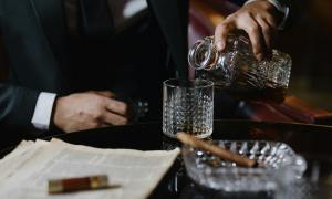 man in black suit pouring drink on glass with cigar in ashtray