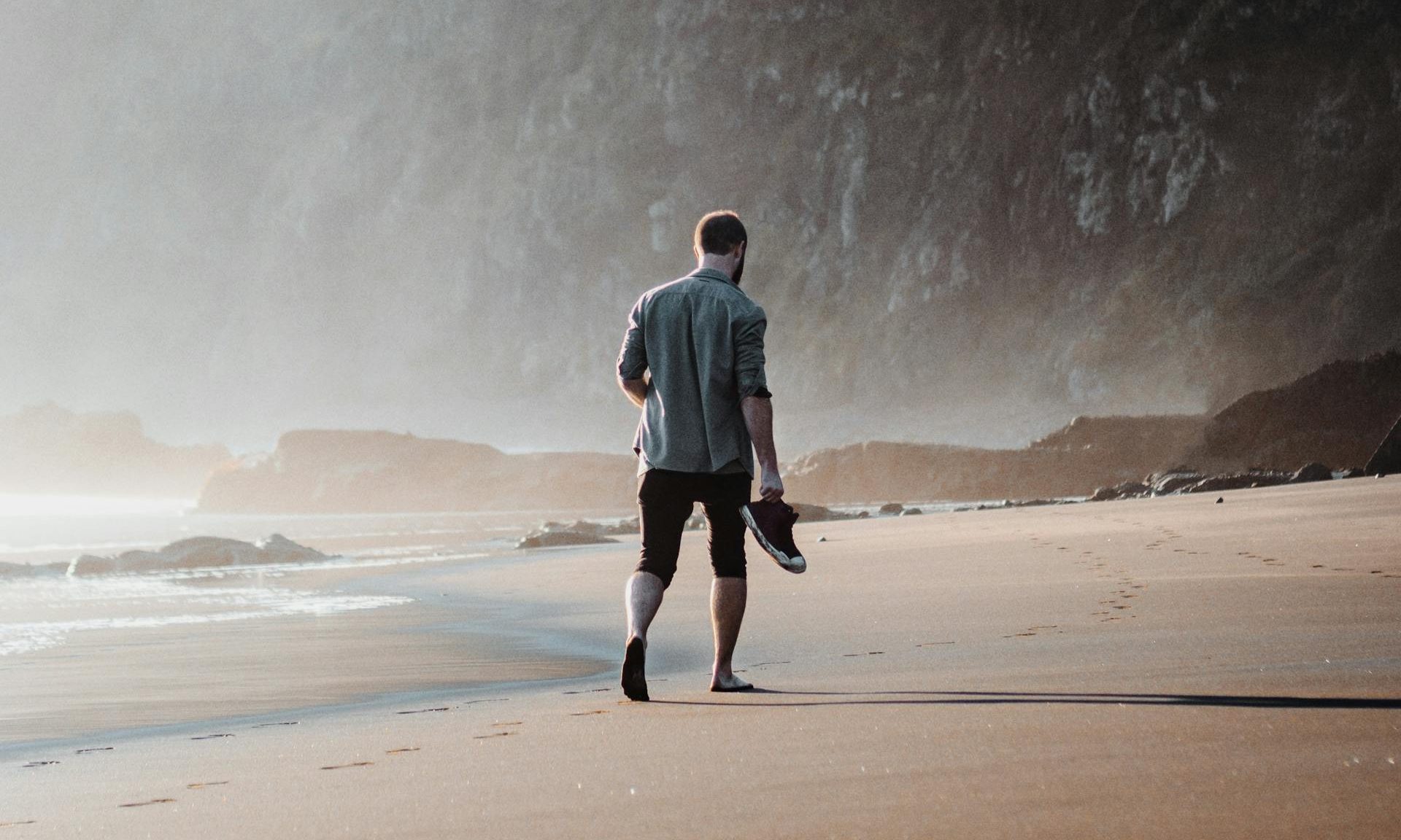 man walking barefoot on sand outside