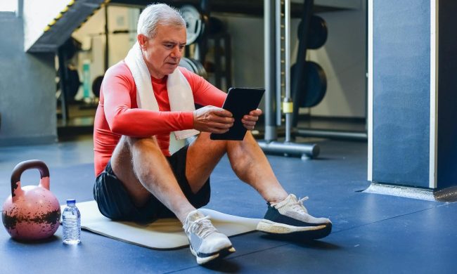 older man sitting in gym ipad kettlebell