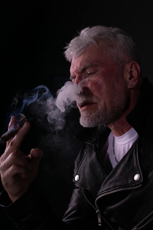 close-up shot of an elderly man in black leather jacket smoking a cigar