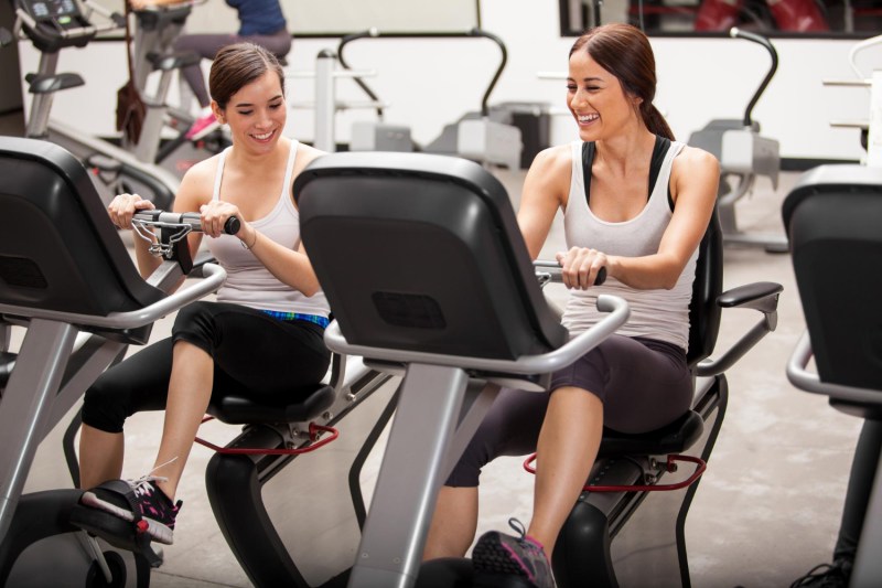 Two women on recumbent bikes in gym.