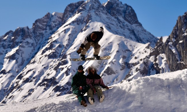 snowboarder jumping over two friends holding beers