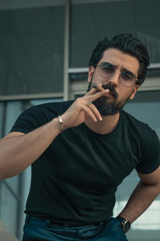 a man with a beard and glasses smoking a cigar