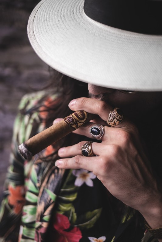 man in hat wearing multiple rings smoking a cigar