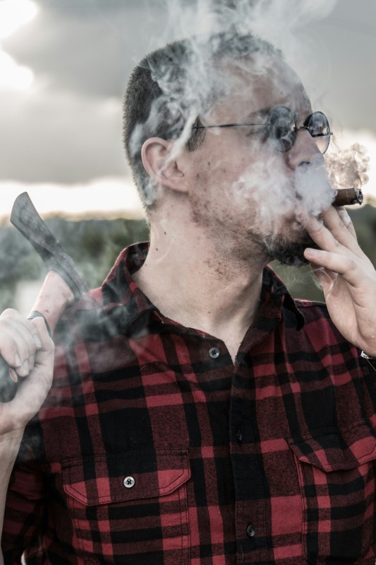 bespectacled man in plaid shirt smoking outside