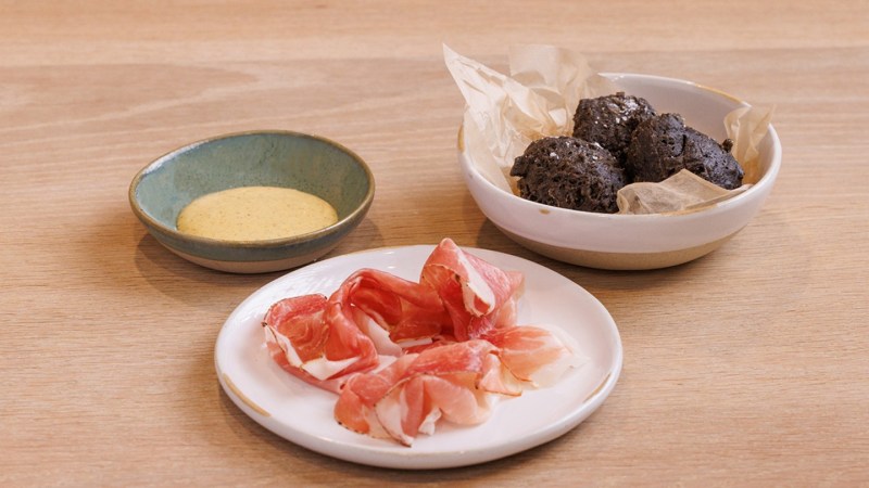 Squid ink biscuits served with speck ham and creole mustard