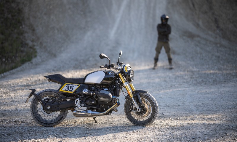 2026 BMW R 12 NineT with Tracker package parked on gravel right profile rider in background.