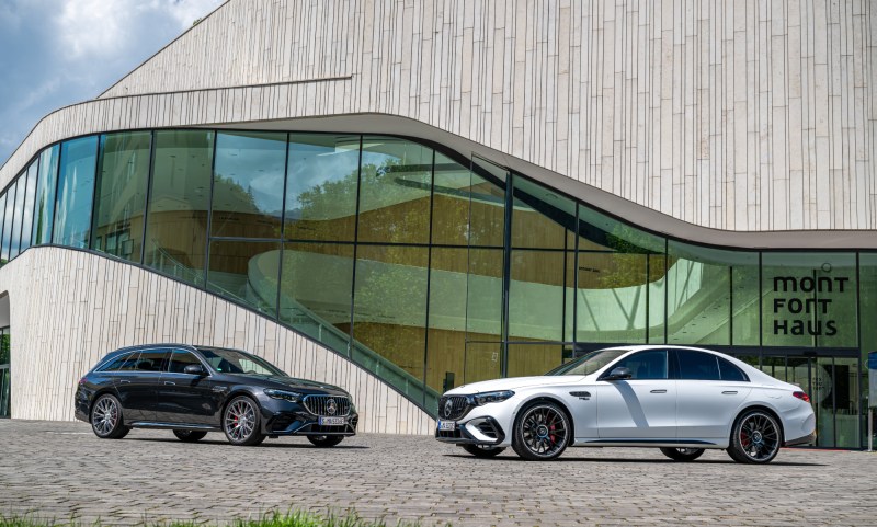 2026 Mercedes AMG E 53 Hybrid black wagon and white sedan facing each other in front of an office building.
