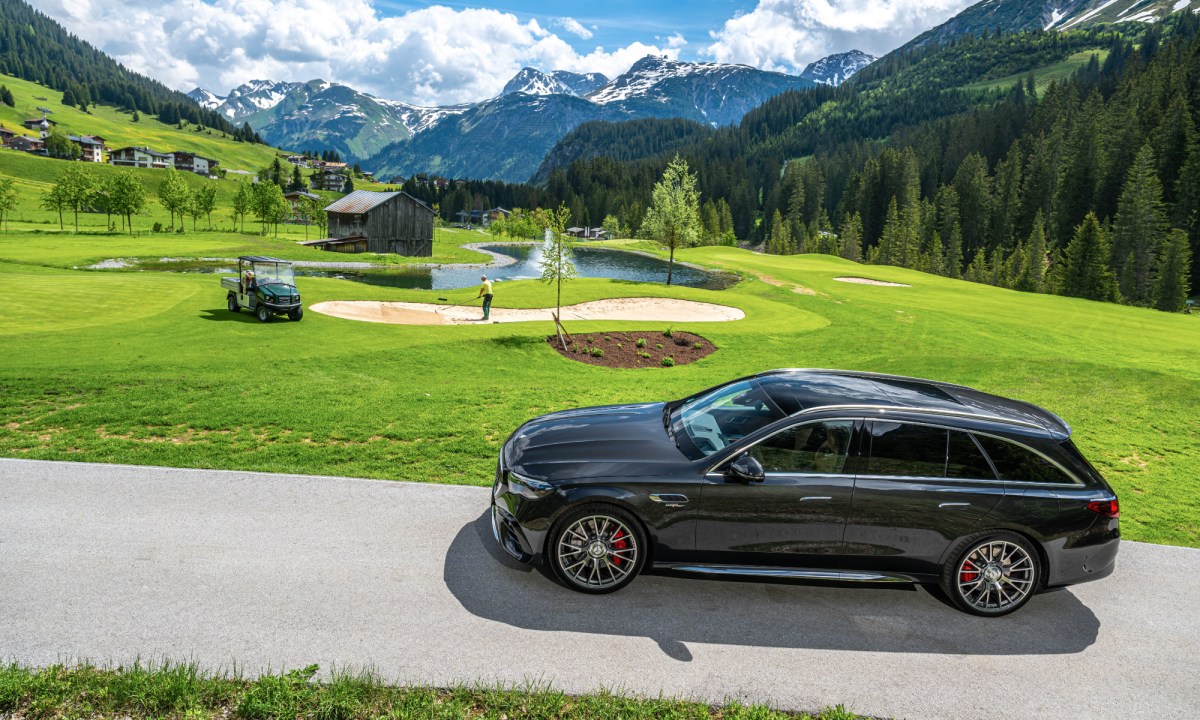 2026 Mercedes AMG E 53 Hybrid wagon left side view driving on a road through a gold course.