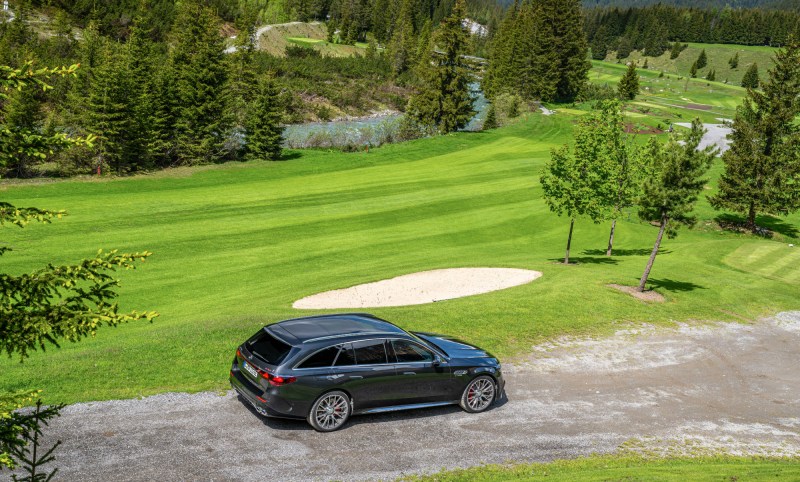 2026 Mercedes AMG E 53 Hybrid wagon right side view driving on a dirt road through a gold course.