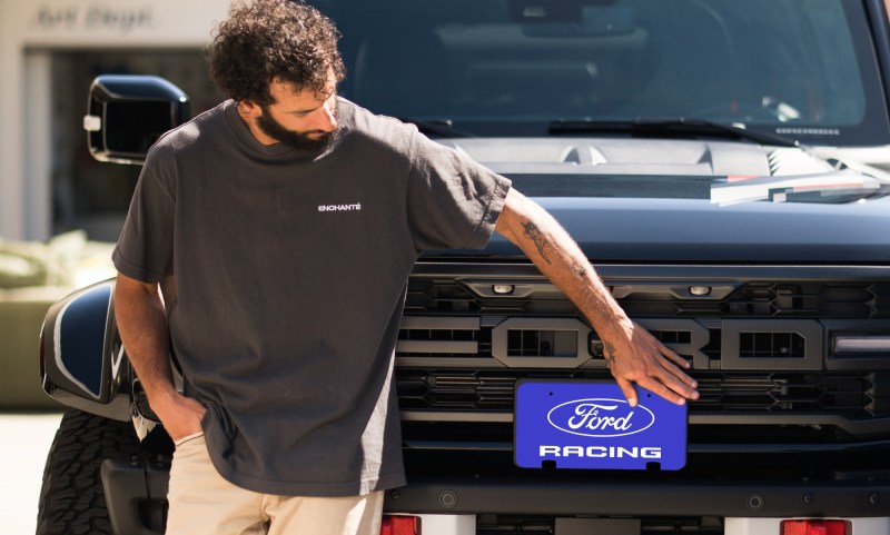 Daniel Ricciardo leaning on a Ford Bronco Raptor looking down at Ford Racing plate.