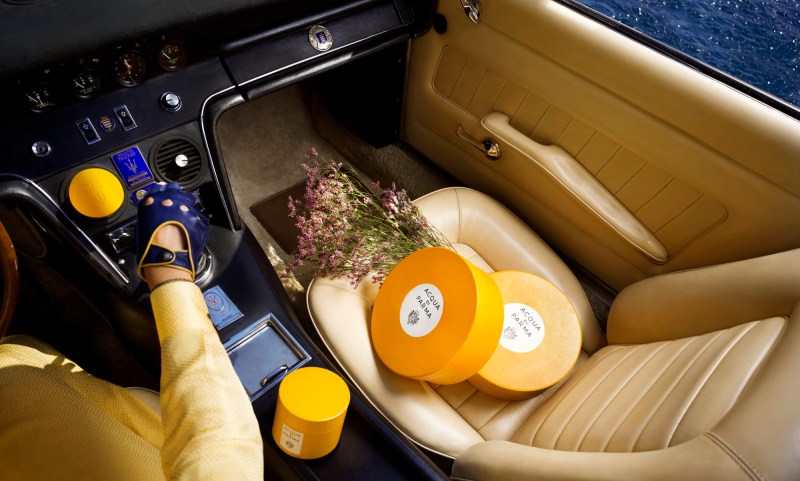 Model sitting in a Maserati Ghibli Spyder with the Acqua di Parma Art of Travel Kit on the passenger seat.