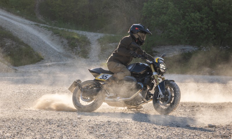 Rider on 2026 BMW R 12 NineT with Tracker package scrambling on gravel.