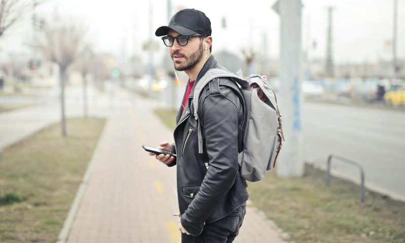 man walking in city holding phone headphones